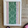 A pea green and baby pink framed textile wall art shown on rush matting.