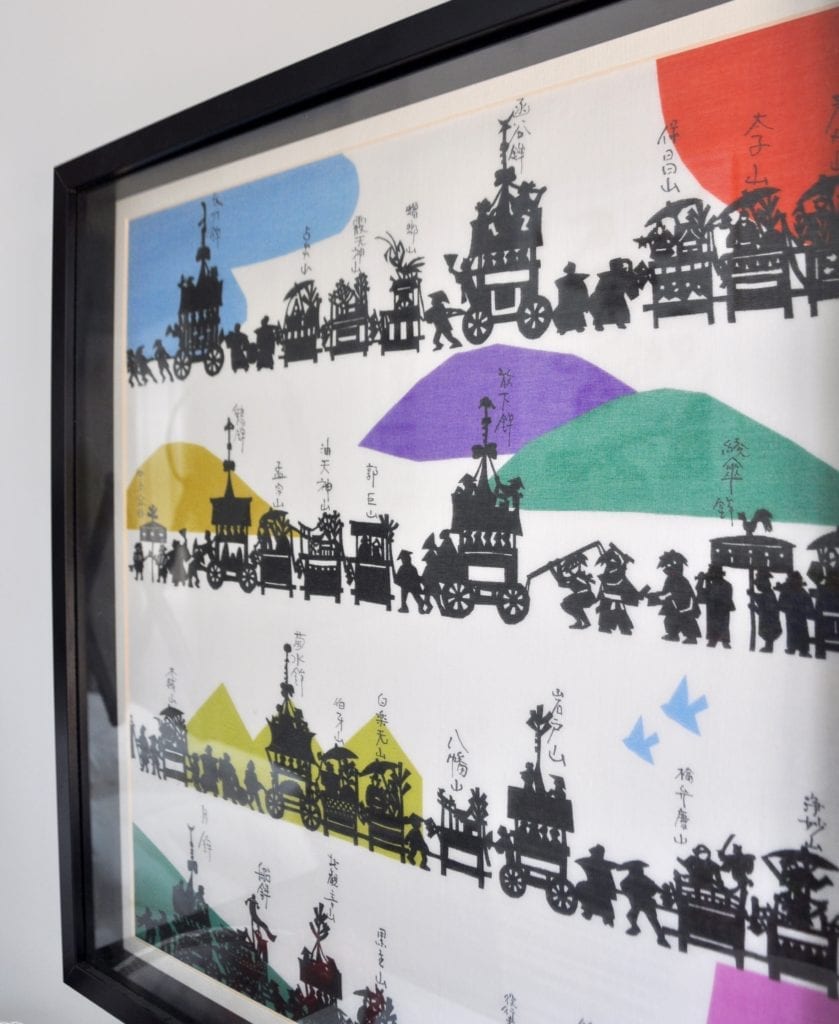 A colourful, Japanese silkscreen print depicting the Gion festival in a simple, black frame.