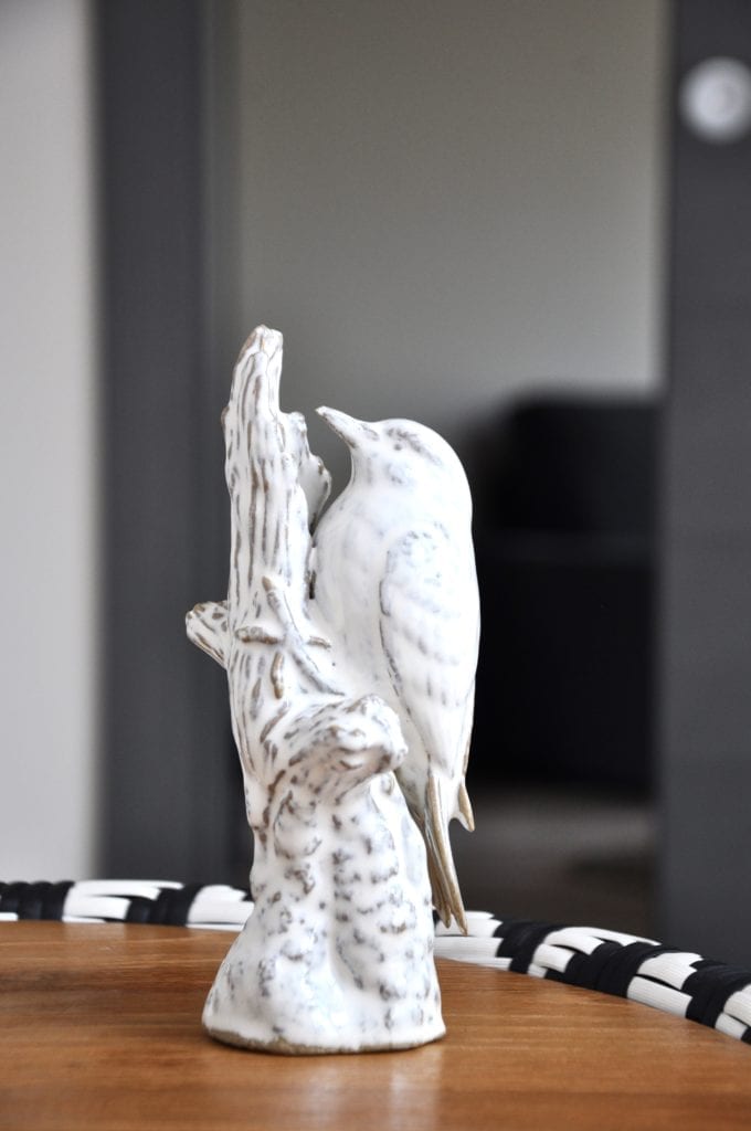 White ceramic bird sculpture on a black, white and wood woven table.