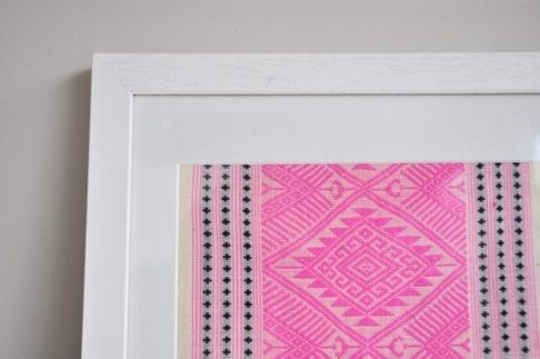 A detail of a framed Thai textile in baby pink, showcasing traditionally-Thai, woven motifs.