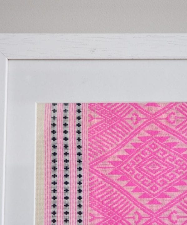 A detail of a framed Thai textile in baby pink, showcasing traditionally-Thai, woven motifs.