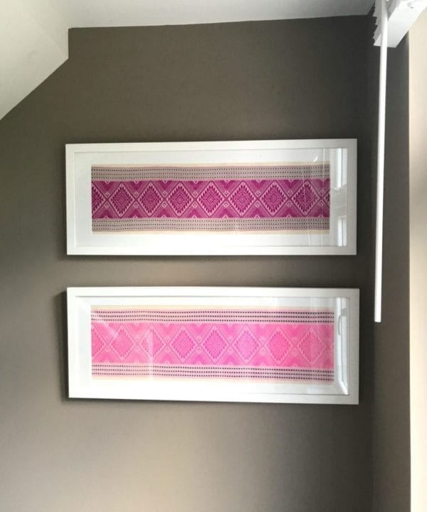 A pair of candy and magenta pink white wood framed textiles hung on a taupe wall by a window.