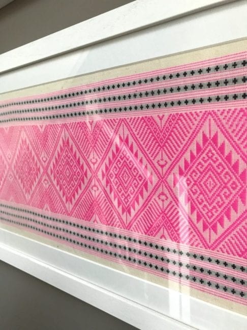 A framed candy pink and navy woven Thai textile.