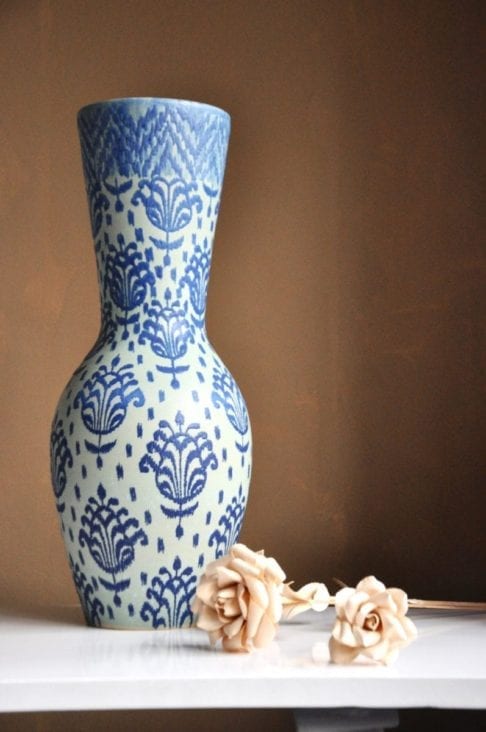 An over-sized, Thai pottery pot displayed against a beige wall with decorative wooden roses.