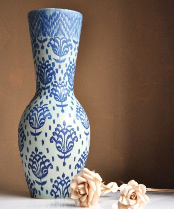 An over-sized, Thai pottery pot displayed against a beige wall with decorative wooden roses.