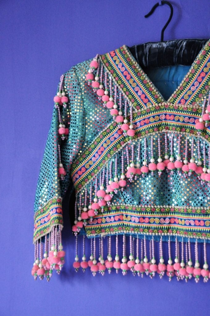 A beaded child's jacket decorated with pink poms. The jacket hails from northern Thailand and was sourced from the Hmong hill tribe textile markets in Chiangmai.