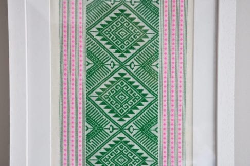 Detail of a framed textile wall art piece in pea green with candy pink accents. The textile was hand-loomed in northern Thailand.