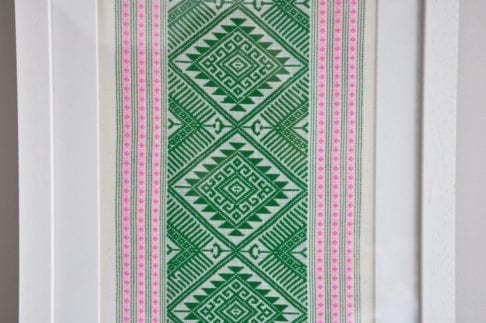 Detail of a framed textile wall art piece in pea green with candy pink accents. The textile was hand-loomed in northern Thailand.