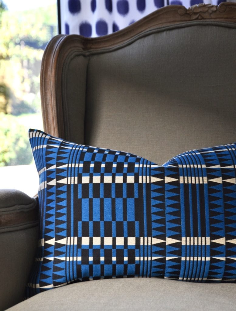 A blue geometric cushion with an African, tribal-pattern-inspired design on a French armchair.