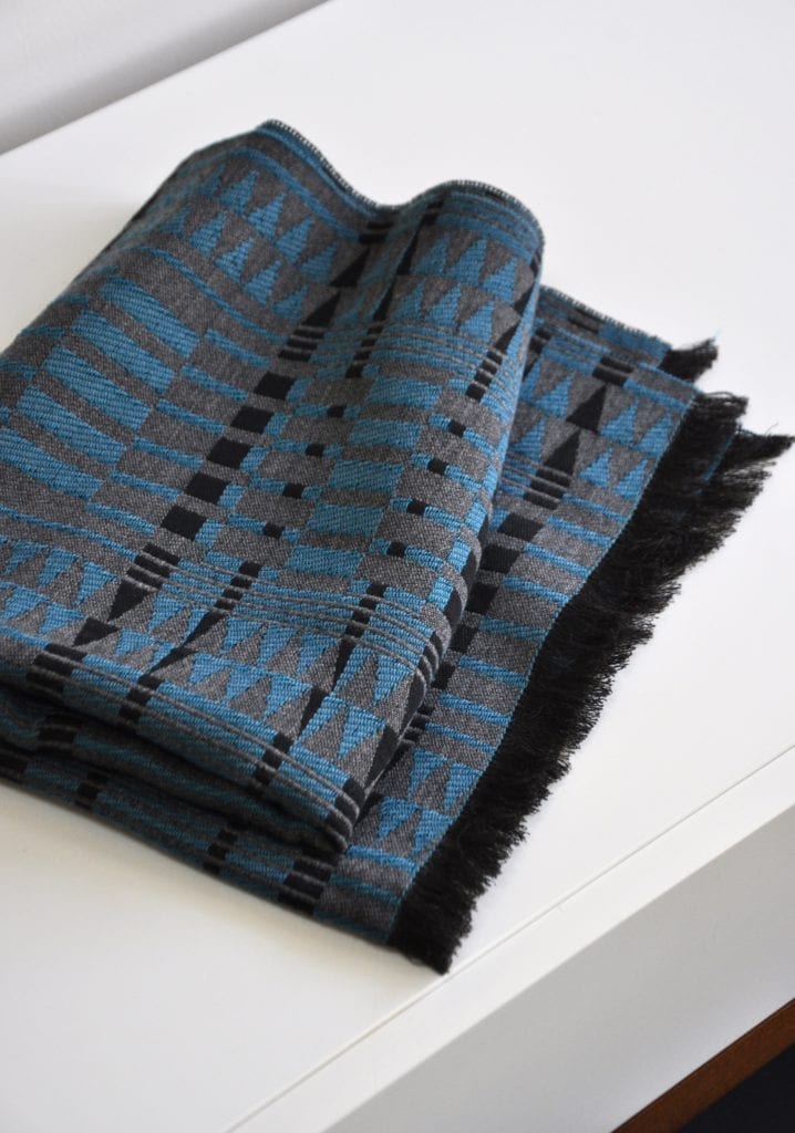 A luxury cashmere mix scarf woven in an African-inspired pattern in shades of grey and blue with a fringed edge.