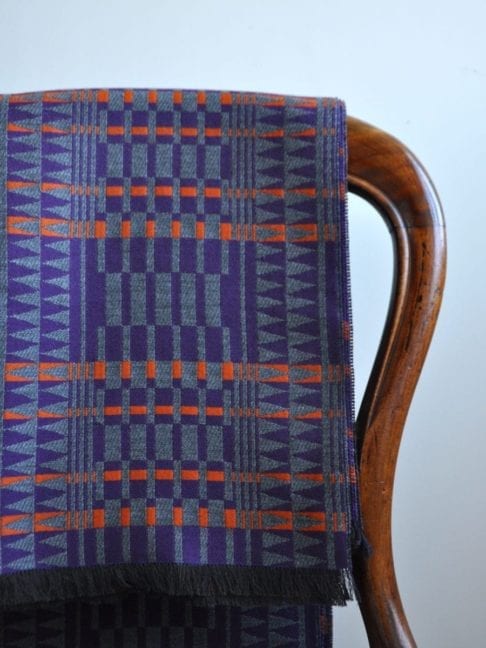 A purple, orange and grey, fringed wrap scarf in the softest cashmere hung on the back of an antique, balloon back dining chair.