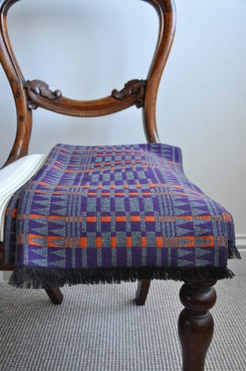 Purple cashmere wrap scarf with orange accents on a vintage chair.