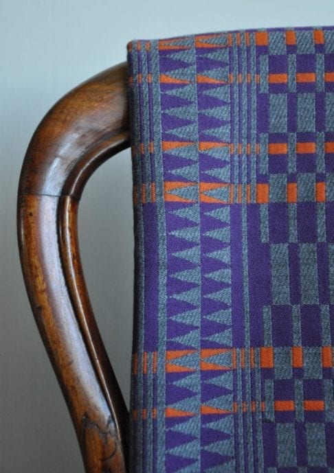 A detail of a cashmere scarf in an African-inspired geometric print in purple, grey and orange, hung on an antique chair back.