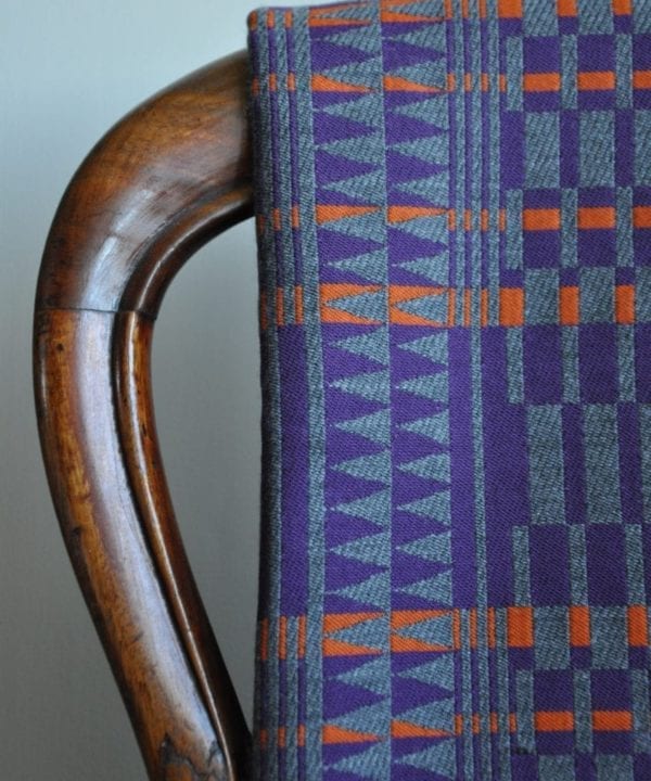 A detail of a cashmere scarf in an African-inspired geometric print in purple, grey and orange, hung on an antique chair back.