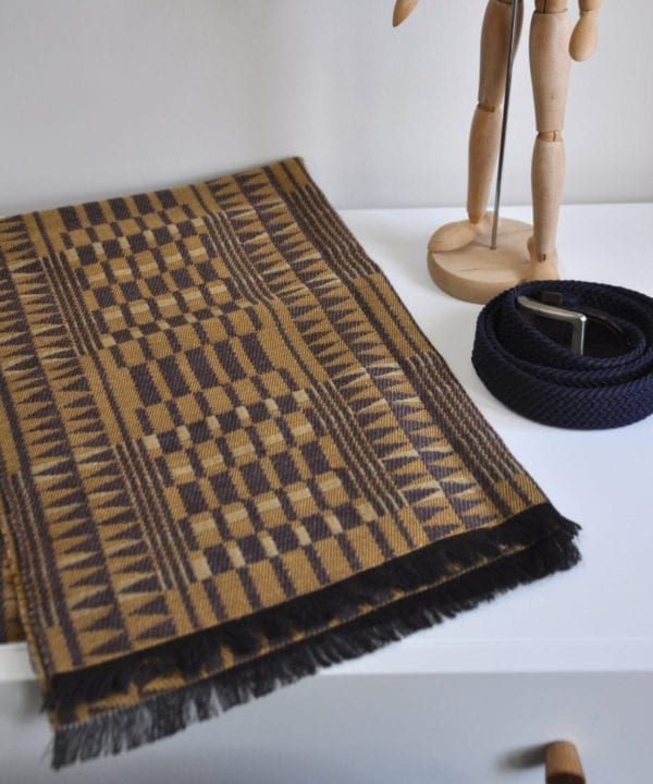 A geometric-weave, cashmere scarf in beiges and browns on a modern, white dressing table.