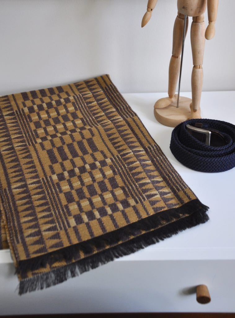 A geometric-weave, cashmere scarf in beiges and browns on a modern, white dressing table.