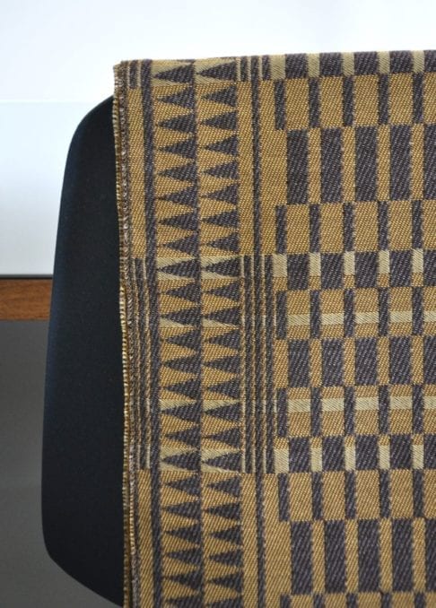 Detail of a geometric-weave, cashmere scarf in beiges and browns, hung on the back of a chair.