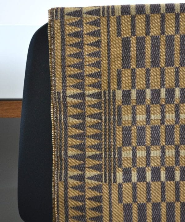 Detail of a geometric-weave, cashmere scarf in beiges and browns, hung on the back of a chair.