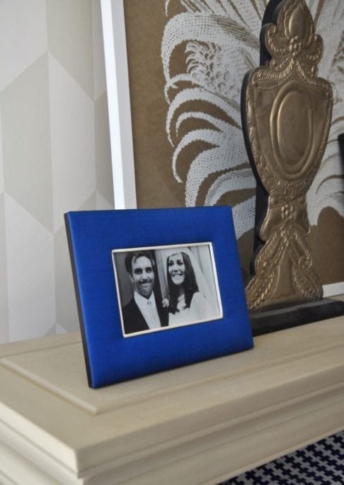 A Thai-silk, Royal blue, photograph frame with a family wedding picture on a neutral-hued bookshelf.