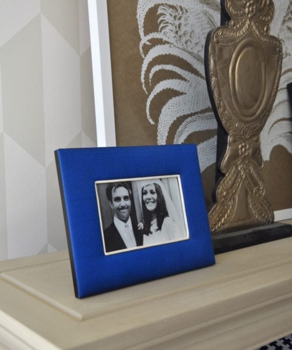 A Thai-silk, Royal blue, photograph frame with a family wedding picture on a neutral-hued bookshelf.