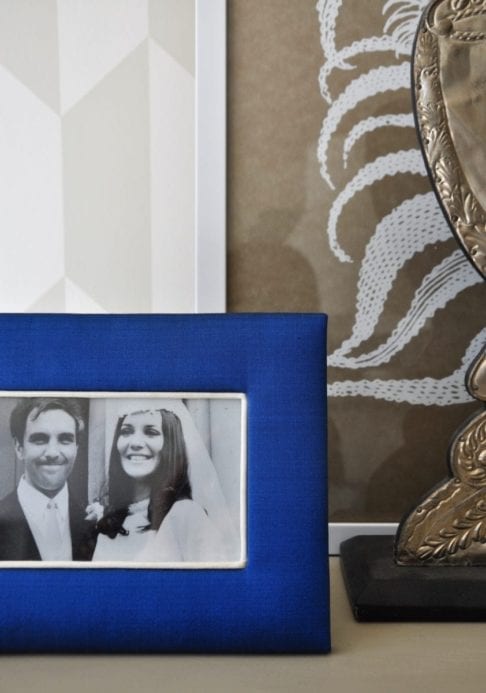 A Thai -silk, Royal blue, photograph frame with a family wedding picture on a neutral-hued bookshelf.