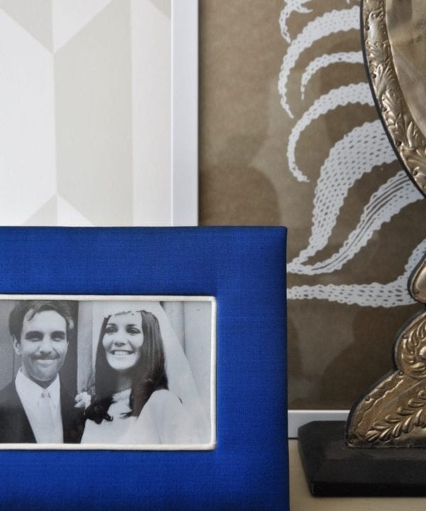 A Thai -silk, Royal blue, photograph frame with a family wedding picture on a neutral-hued bookshelf.