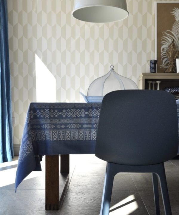 Luxury, patterned, blue linen tablecloth with Arabian motifs on a modern, wooden dining table in a stylish room setting with oversized pendant and geometric wallpaper.