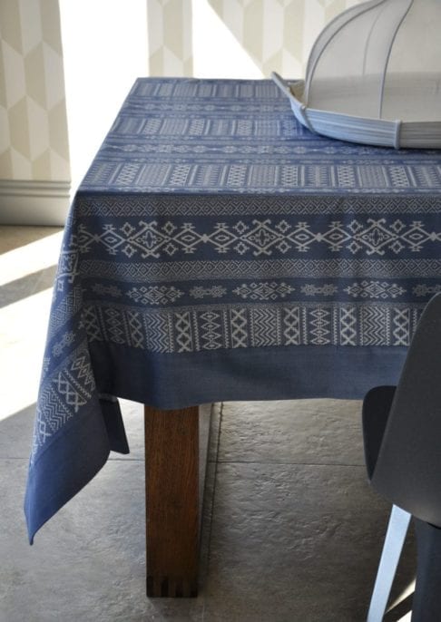 Luxury blue linen tablecloth with Arabian architectural motifs in the weave, shown on a modern, wooden dining table.