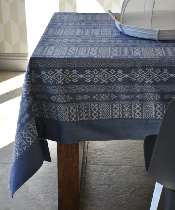 Luxury blue linen tablecloth with Arabian architectural motifs in the weave, shown on a modern, wooden dining table.