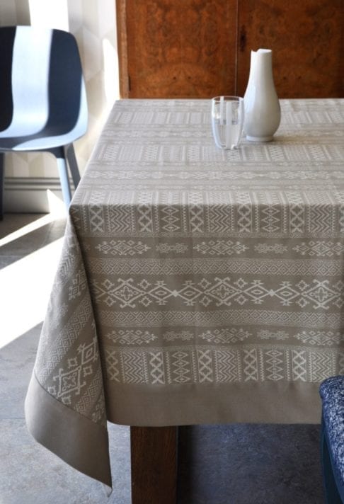 Overhead shot of our neutral tablecloth with subtle architectural detailing is styled up in a modern dining room setting with blue chair in the background.