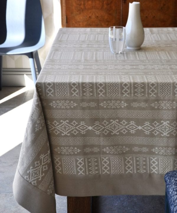 Overhead shot of our neutral tablecloth with subtle architectural detailing is styled up in a modern dining room setting with blue chair in the background.