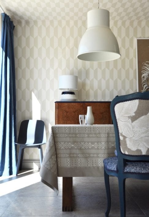 Our neutral tablecloth displayed in an elegant, light-filled dining room in blues and tan with neutral geometric wallpaper, large metal downlighters and French-style upholstered dining chairs.