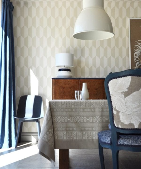 Our neutral tablecloth displayed in an elegant, light-filled dining room in blues and tan with neutral geometric wallpaper, large metal downlighters and French-style upholstered dining chairs.