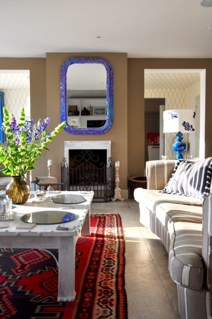 A sunny relaxed, eclectic sitting room wit a Turkish rug, stripy sofa, blue mosaic-tiled mirror and white-washed Indian coffee table.