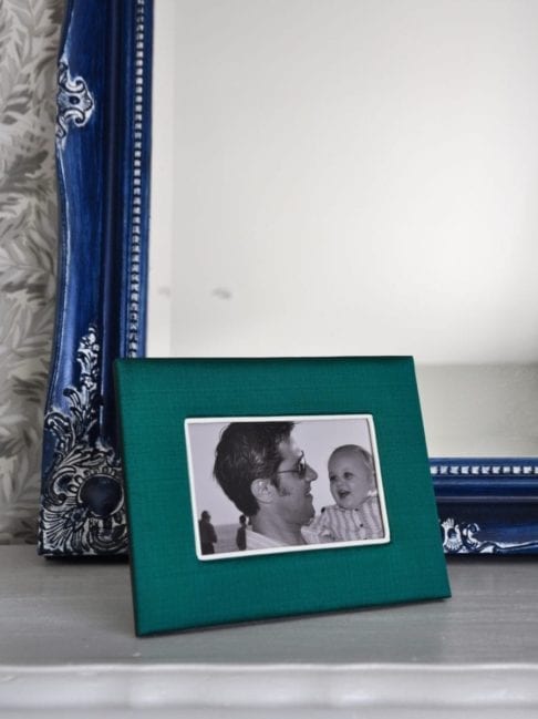 A Thai-silk, emerald green photograph frame with a picture of a parent and baby, against a blue mirror backdrop.