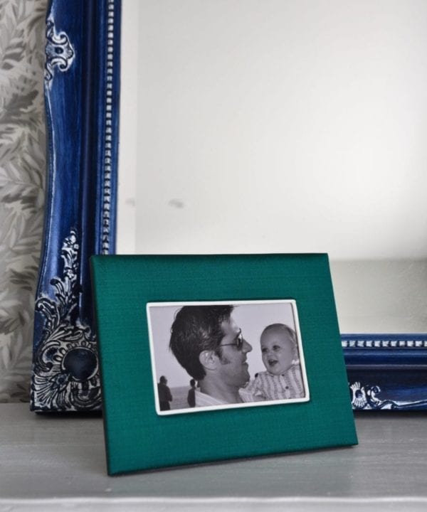 A Thai-silk, emerald green photograph frame with a picture of a parent and baby, against a blue mirror backdrop.