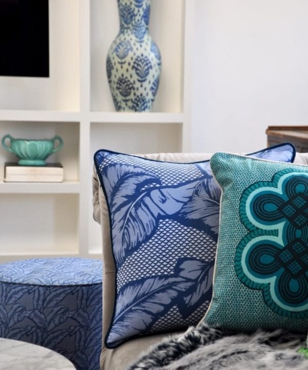 African motif cushion in blue and aqua on a cosy sofa with a faux fur throw and ceramic pots on shelves in the background.