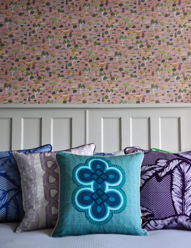 Colourful Ghanaian and Nigerian style cushions grouped on a bed against Aboriginal wallpaper in the background.