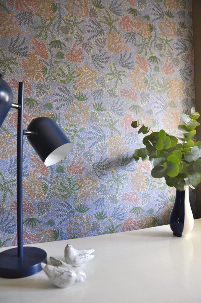 A blue angle poise lamp in foreground with blue floral Aboriginal symbols wallpaper.