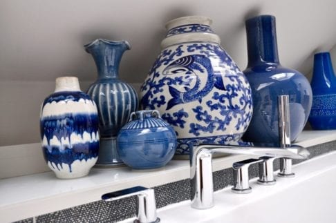 A large blue and white pot surrounded by smaller, decorative pots in the same classic colour combination and styled in a modern bathroom setting.