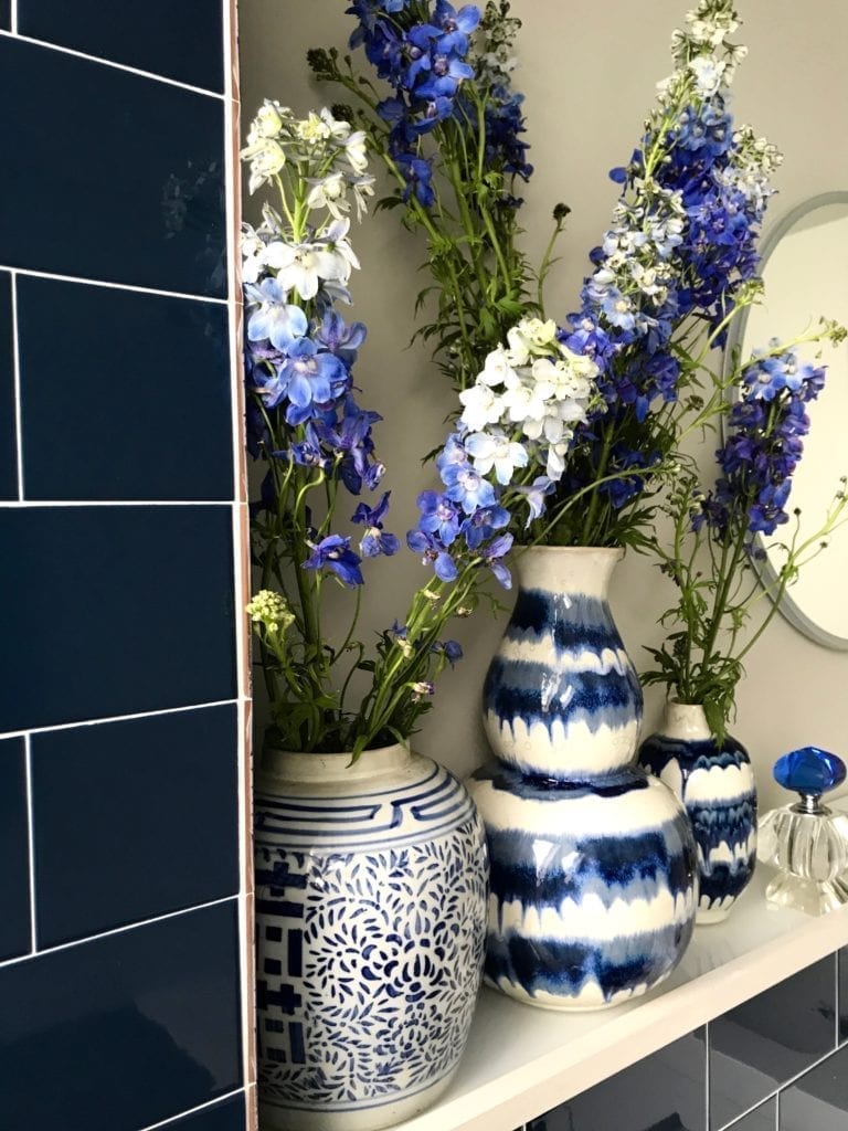 A display of delphiniums in a selection of Asian blue and white china vases in a blue, tiled bathroom.