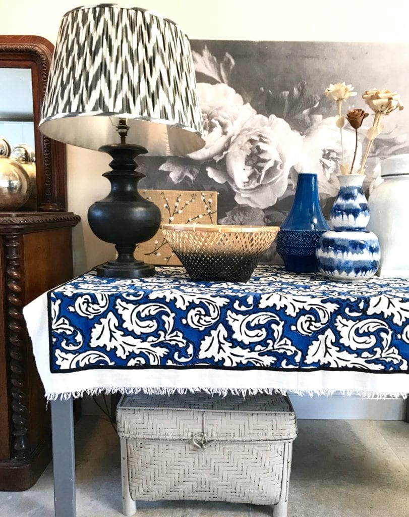 A monochrome and blue sideboard still life display showcasing a large scale Ikat lamp shade with turned wood base, baskets, ceramics and botanical textiles and a large floral canvas of Peony in black and white.