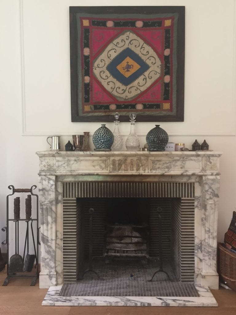 A marble fireplace with a framed central European textile displayed above it.