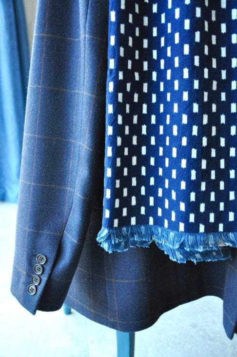 Detail of an indigo blue scarf hung on a tweed check jacket.