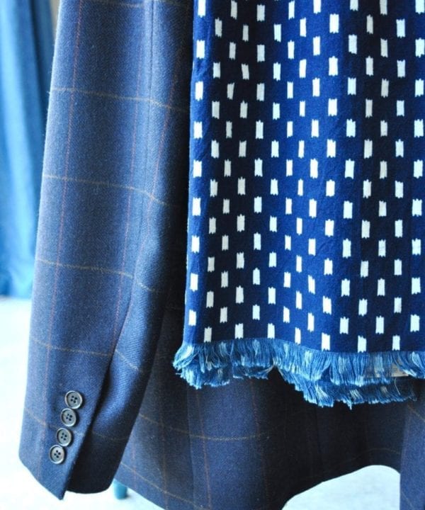 Detail of an indigo blue scarf hung on a tweed check jacket.