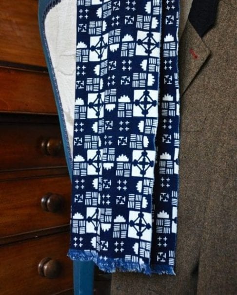 An indigo geometric print scarf on cotton and hung on a tweed jacket with a mahogany chest in the background.