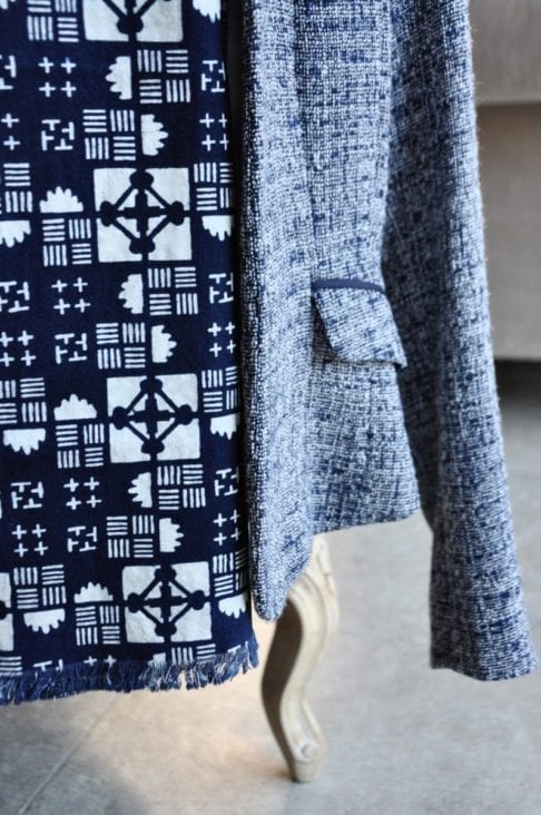 Close-up of a geometric print cotton scarf hung on a ladies blue tweed jacket on a chair.