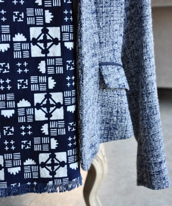 Close-up of a geometric print cotton scarf hung on a ladies blue tweed jacket on a chair.