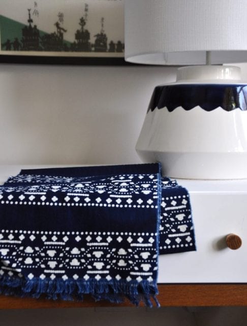 An Asian style indigo stripe scarf on a dressing table with a ceramic table lamp.