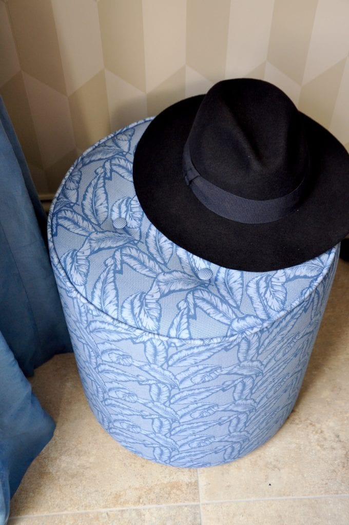 A blue banana leaf print pouffe with a navy, felt Trilby hat on top.